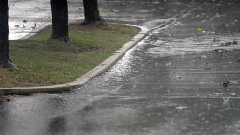 Heavy-rainfall-splashing-on-asphalt-road,-adjacent-to-grassy-curb