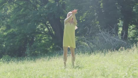 아름다운 젊은 소녀가 자유의 춤을 추고 있습니다. 여름 공원에서 뒷면에 나무가 있습니다.