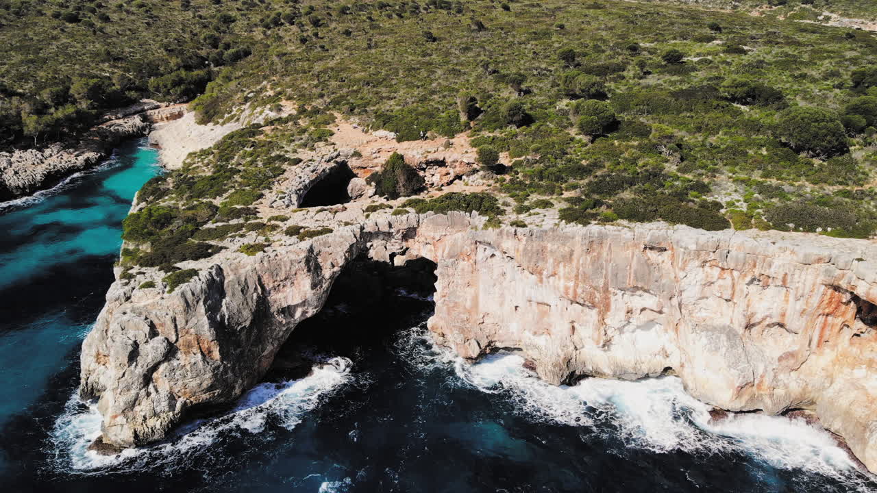 a wide drone shot flying forward towards a large sea arch near cala varques in majorca