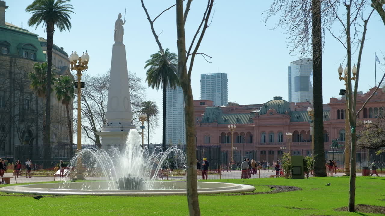 Fountain and people walking in May Square, May Pyramid and Pink House in background at daytime wide shot