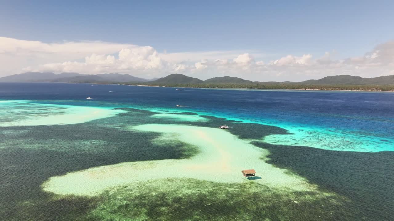 Drone captures Candaraman Sand Bar in Sulu Sea with rustic nipa-style floating hut perched over shallow coral waters, backed by white sandbanks and dense tropical forest, Balabac Island, Philippines