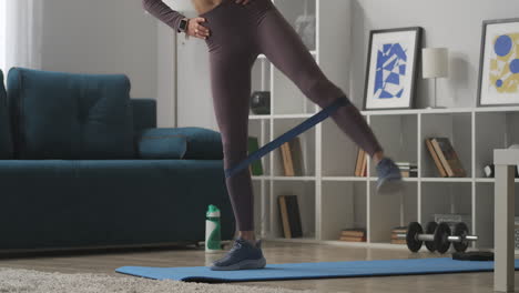 gimnasio en casa en un apartamento moderno mujer está entrenando con banda elástica en las piernas vista de cerca de las partes del cuerpo estilo de vida saludable