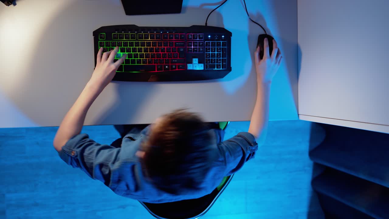 Entertainment at home. View from above on a boy playing on his computer. Teenage boy sitting at the desk and pressing the buttons on a keyboard. Top view.