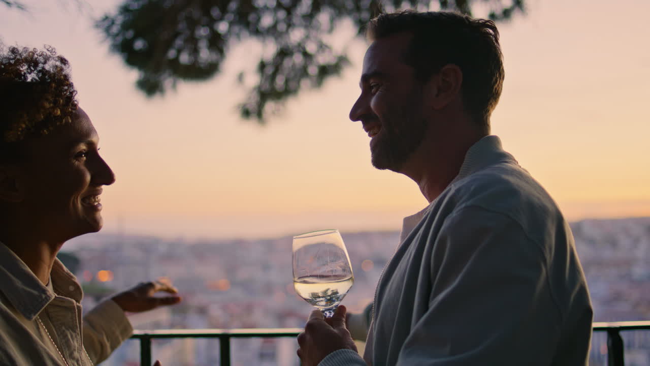 Primo piano di sagome di innamorati che ridono su una terrazza con vista al tramonto. Appuntamento di coppia spensierato.