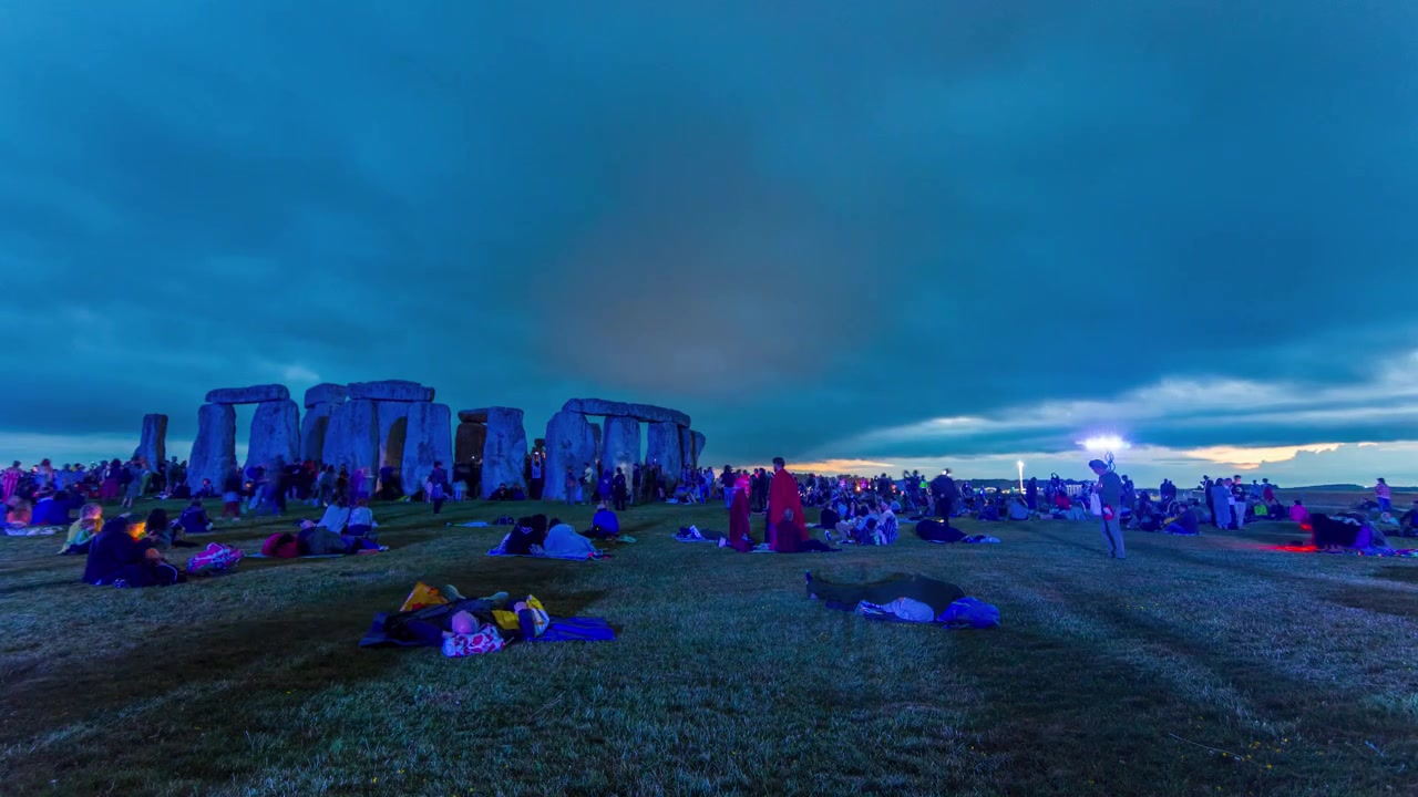 Ampia inquadratura di folle che riposano e si accampano a terra a Stonehenge durante la notte, in attesa dell'alba del solstizio.