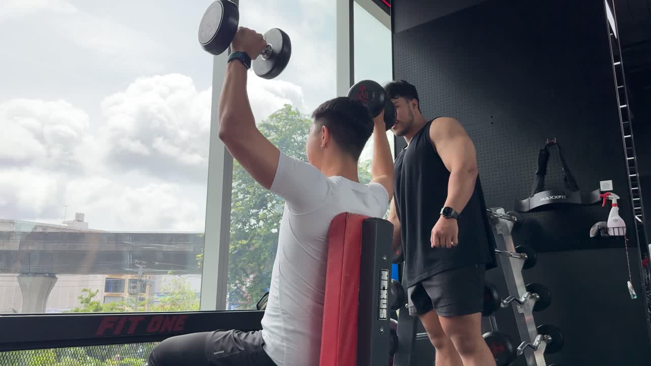 Two men engage in a weightlifting session with a trainer guiding exercises in a well-lit gym