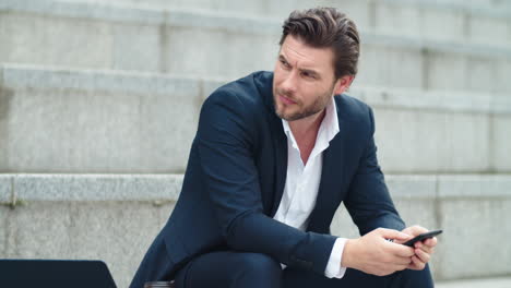 worried business man sitting on stairs. male entrepreneur holding smartphone