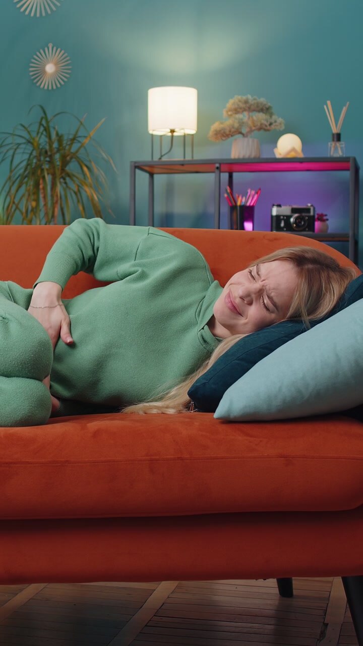 Sick ill woman suffering from period cramps stomach ache menstrual pain lying on sofa at home room