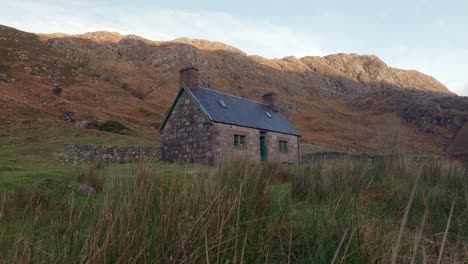 elevándose lentamente de la vegetación en primer plano revela un antiguo edificio de piedra en la base de una montaña en una cañada remota en la escocia rural