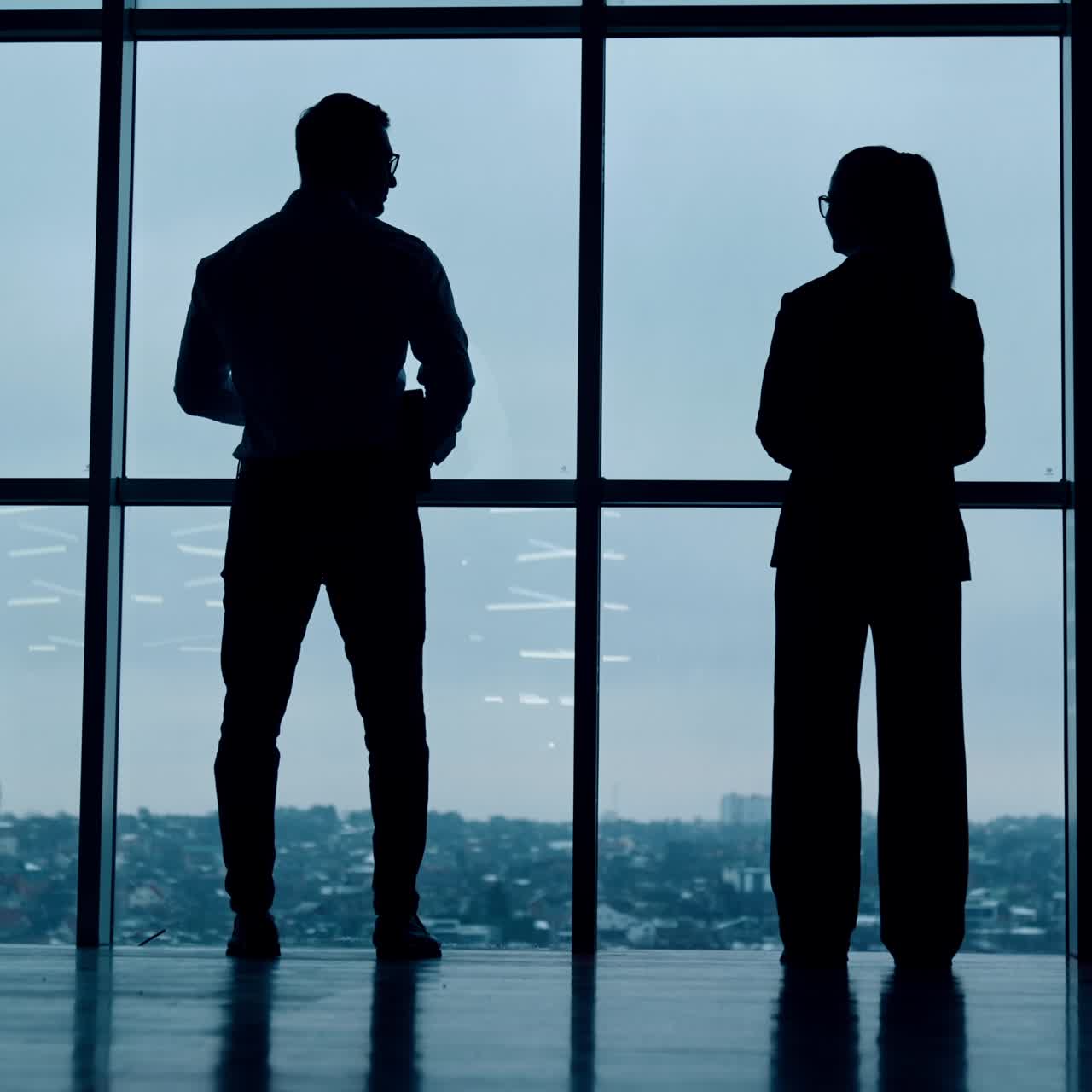 Two full-length silhouettes standing at the window. Male and female stand back to the camera looking at panoramic window