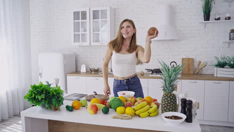 joyful woman with coconut in the kitchen. attractive female is dancing with fresh coconut on the background of organic fruit and vegetables. healthy lifestyle. vertical video