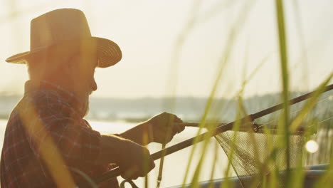 rear view of a caucasian fisherman with a hat catching a fish and taking it out of a net in the lake in the morning