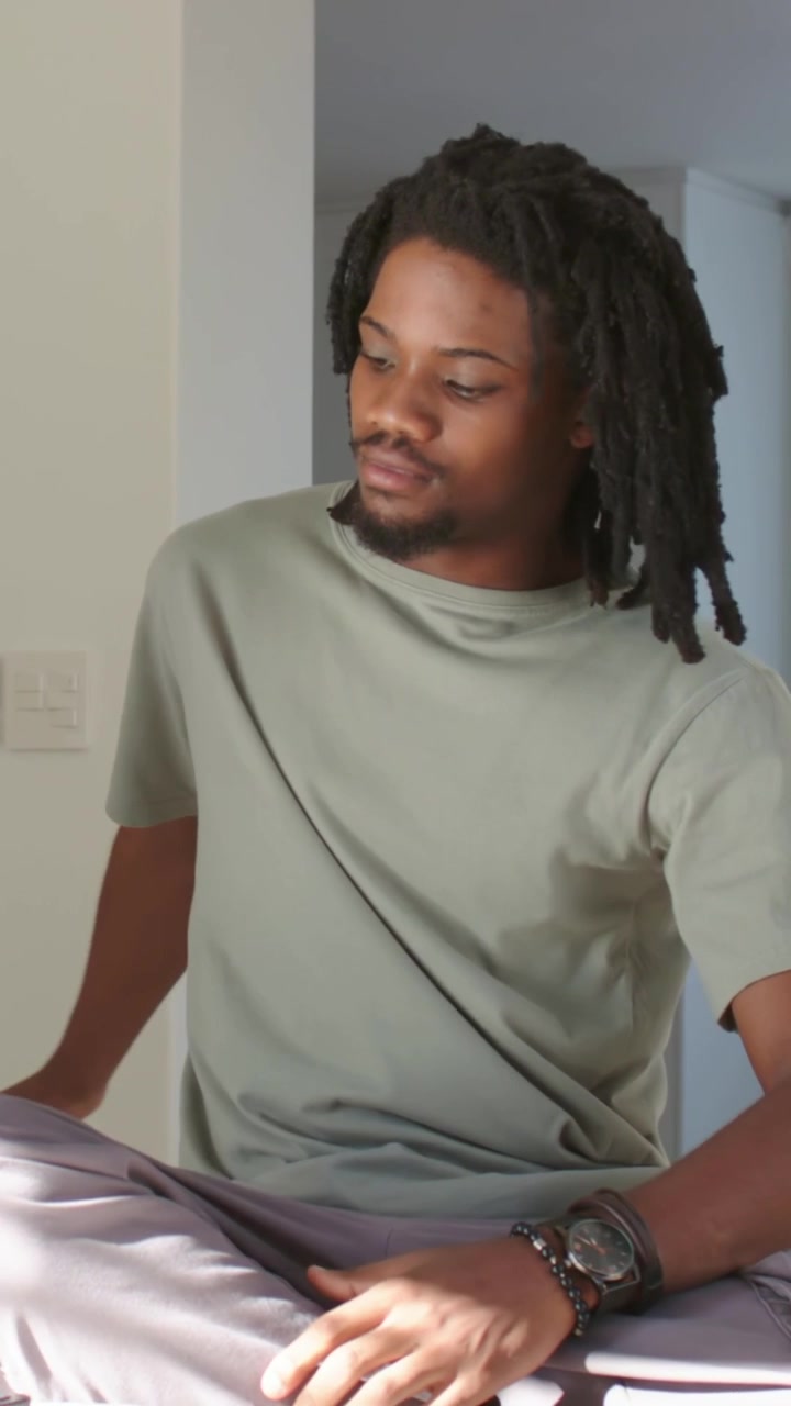 Vertical video: Reaching left man in green tee picking white object in room shifting and looking