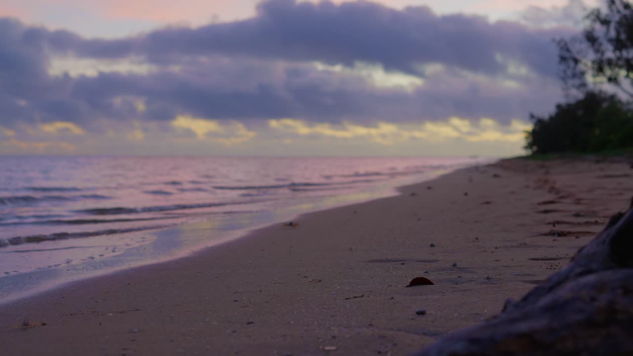 una puesta de sol en una playa abandonada con un tronco en el medio