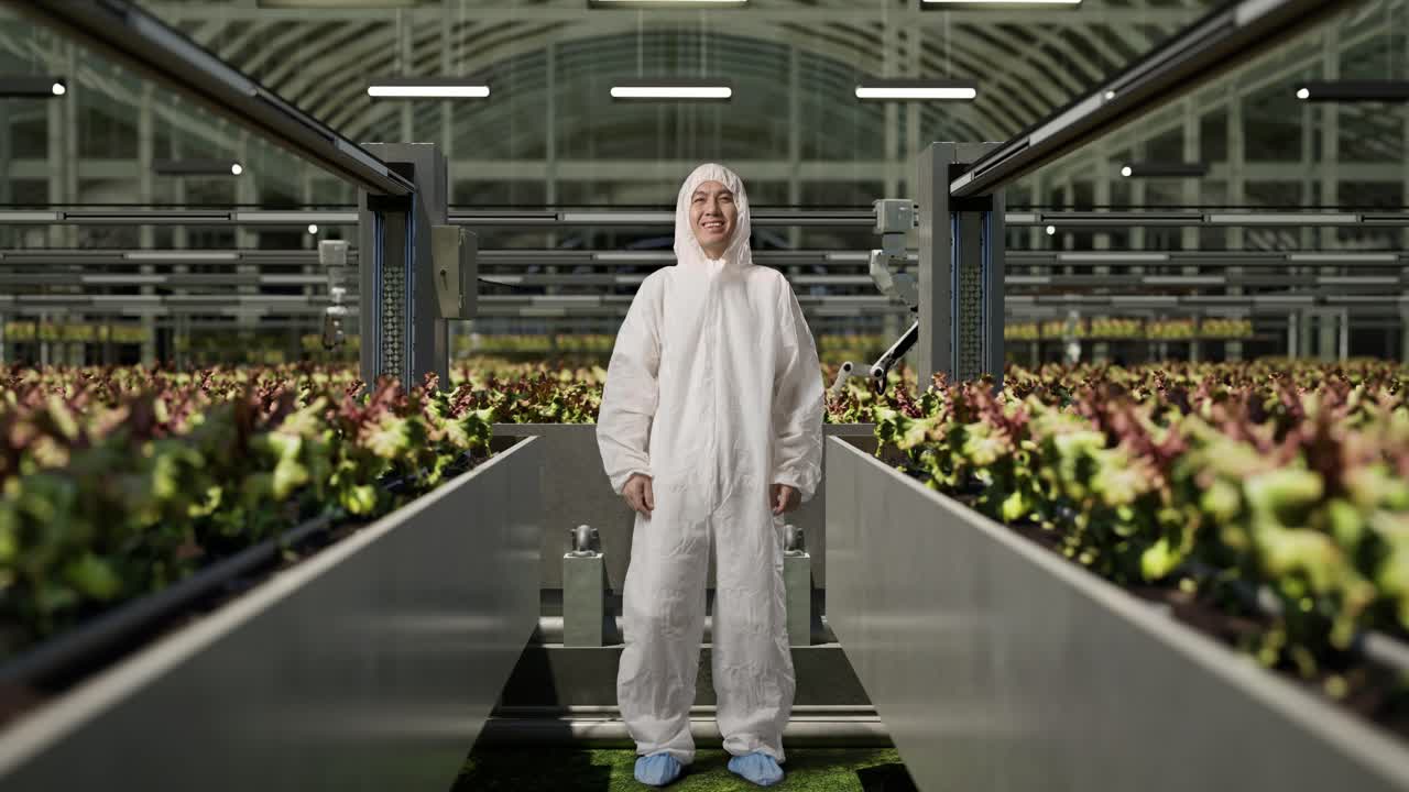 полное тело азиатского человека исследователь смотрит в камеру и улыбается, стоя в теплице с умными роботами-фермерами