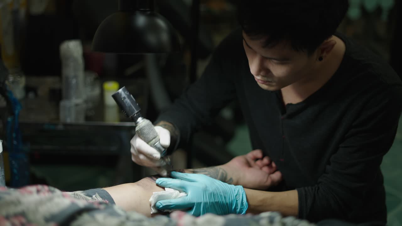 A tattoo artist working on a client's arm in a tattoo studio