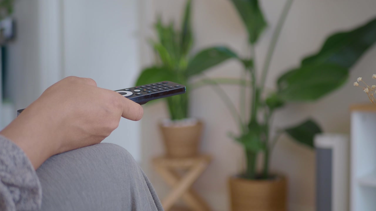 Close-up of Hand Holding TV Remote Control and Pressing Button