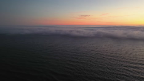 aerial view tilting over the sea, revealing a wall of coastal fog, haar or seafret, during dusk