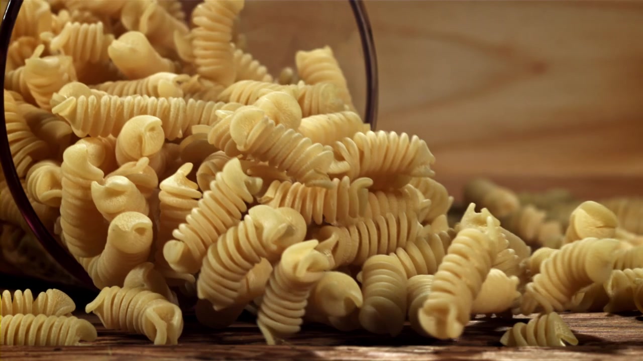 Fusilli secchi che fuoriescono da un contenitore di vetro su un tavolo di legno
