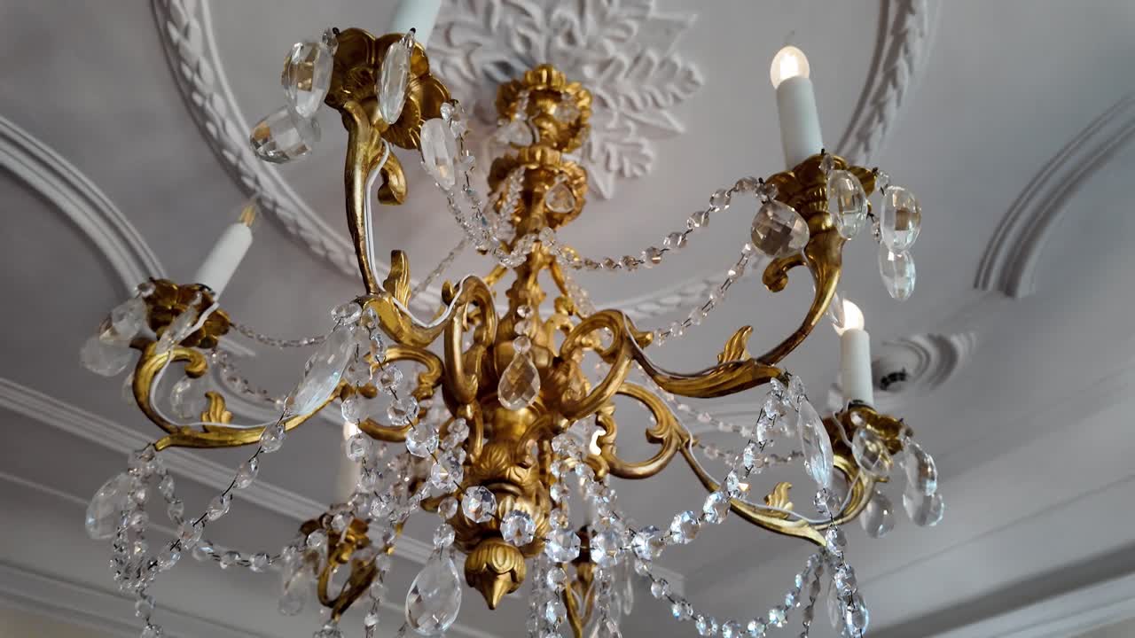 Elegant gold chandelier with six candle arms and crystal ornaments hanging in a medieval castle chamber. Warm glow, historic ambiance, and noble craftsmanship in vintage interior