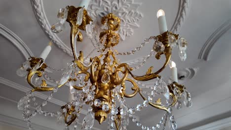 elegant gold chandelier with six candle arms and crystal ornaments hanging in a medieval castle chamber. warm glow, historic ambiance, and noble craftsmanship in vintage interior