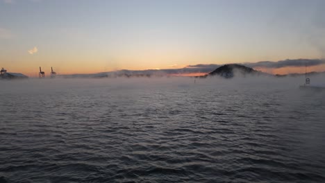 mist rising from water near bjorvika, oslo with golden hour sunset on horizon