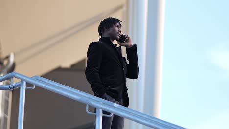 african businessman under modern building roof in outdoor phone call