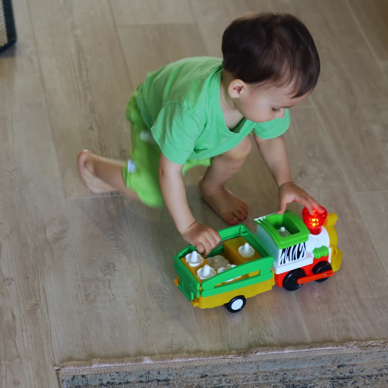 Caucasian toddler puts his toy car on batteries on the side. Kid watches how the wheels move. Top view