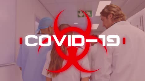 Das-Wort-„Covid-19“-Steht-Auf-Einem-Gesundheitsgefährdungsschild,-Im-Hintergrund-Gehen-Wissenschaftler-Durch-Ein-Krankenhaus