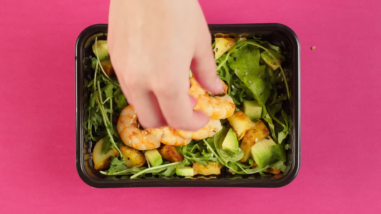 Hand Adding Shrimp to Fresh Salad in Takeaway Container