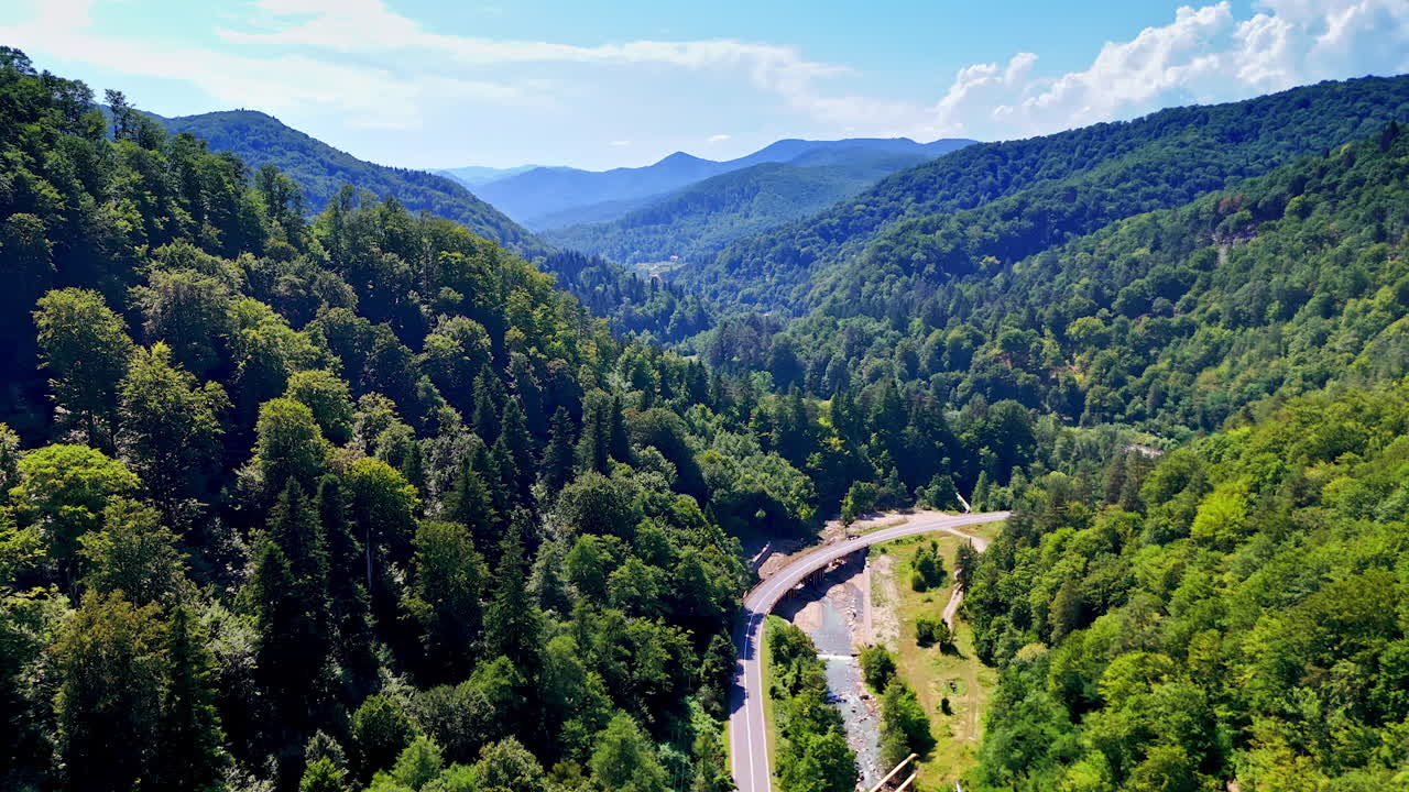 Curved road along a mountain stream. Aerial perspective of a winding road following a river through forested valley in Romania