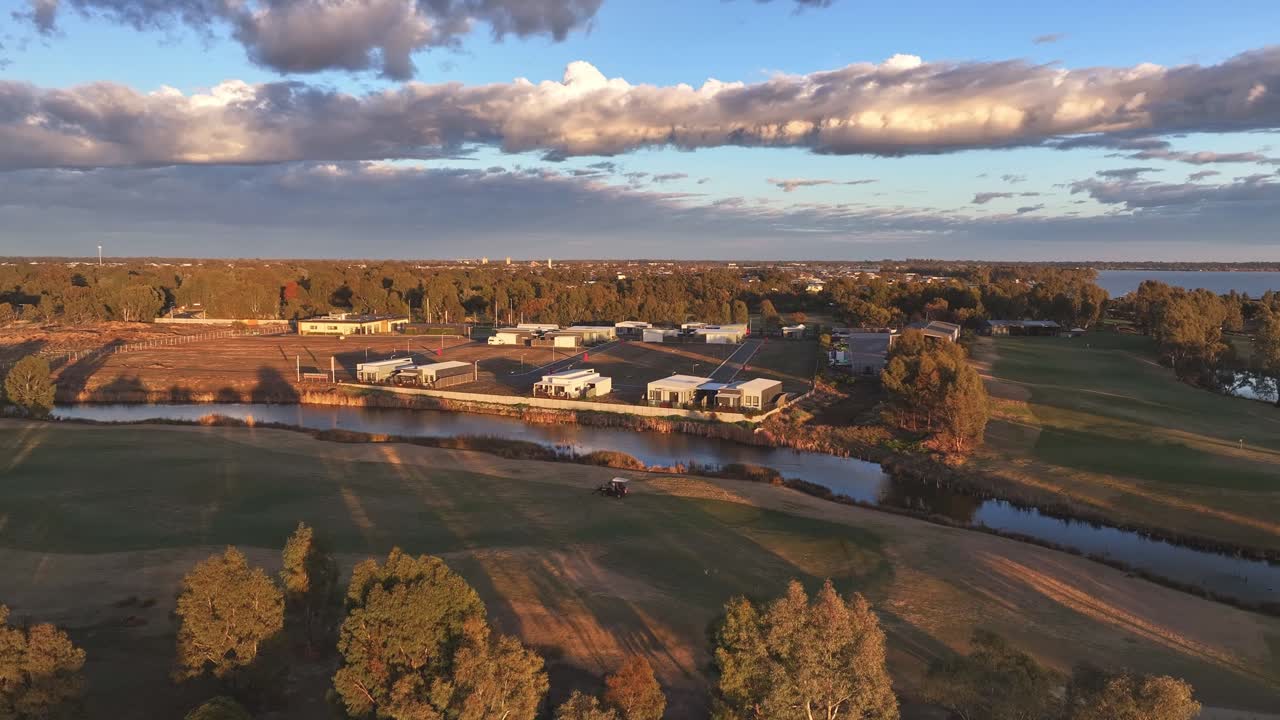 Golf course and cabins cast long shadows in golden hour sun by a winding creek