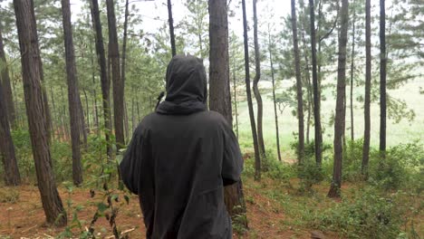 Tracking-shot-from-behind-following-an-African-hunter-with-a-bow-and-arrow-and-wearing-a-hooded-cloak-while-walking-through-a-forest