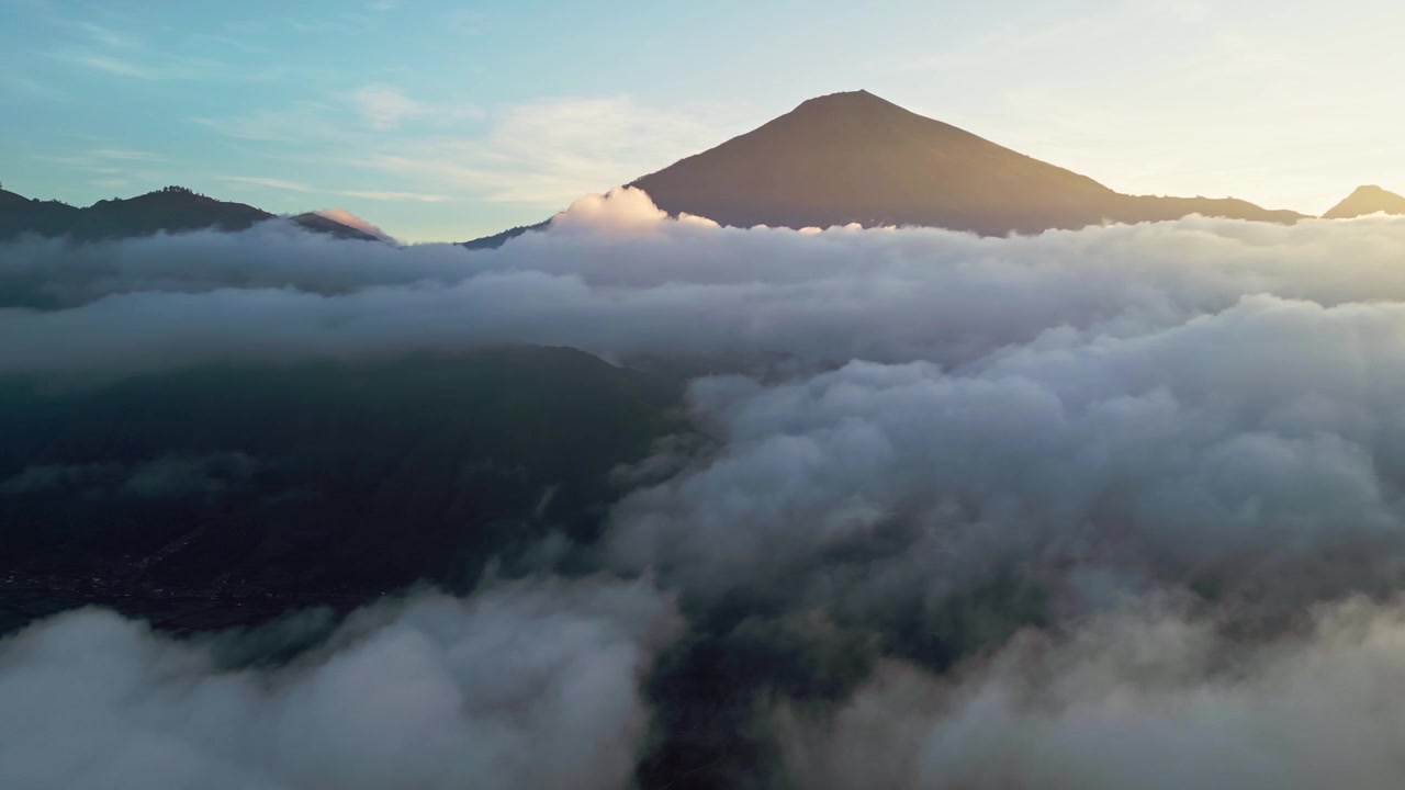 Inversione di nuvole che circonda un'imponente montagna vulcanica illuminata dalla luce dorata dell'alba sopra un mare di nuvole, filmato aereo da drone.