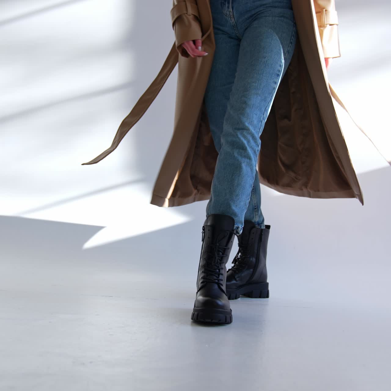 Massive black army boots with laces on a model wearing jeans and beige coat. Lady walks and turns on the white floor
