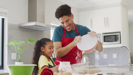 Happy-biracial-father-and-daughter-baking-together-in-kitchen