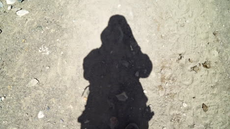 pov shot filming own shadow as walking on a dirt road, a hiker in nature, with the feet in the frame, looking down