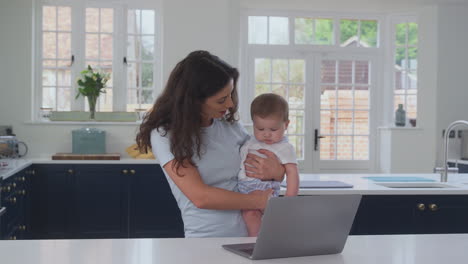 Madre-Con-Hijo-Trabajando-Desde-Casa-En-Una-Computadora-Portátil-En-La-Cocina