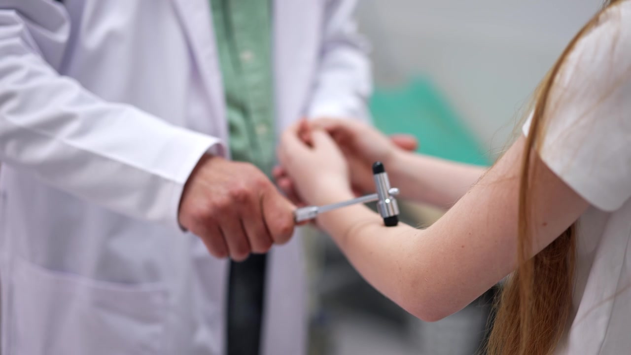 Médico não identificado vestindo jaleco branco usa um martelo no paciente. Exame neurológico no hospital.
