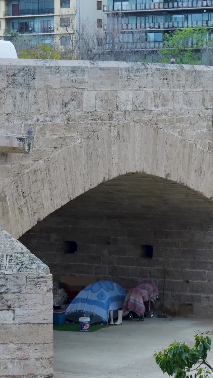 Homeless encampment under a stone arch bridge in an urban setting
