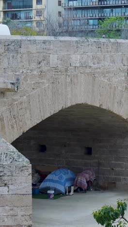 homeless encampment under a stone arch bridge in an urban setting