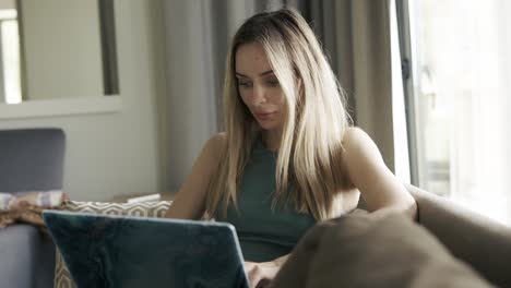 Concentrated-woman-sitting-on-sofa-browsing-social-media-on-laptop