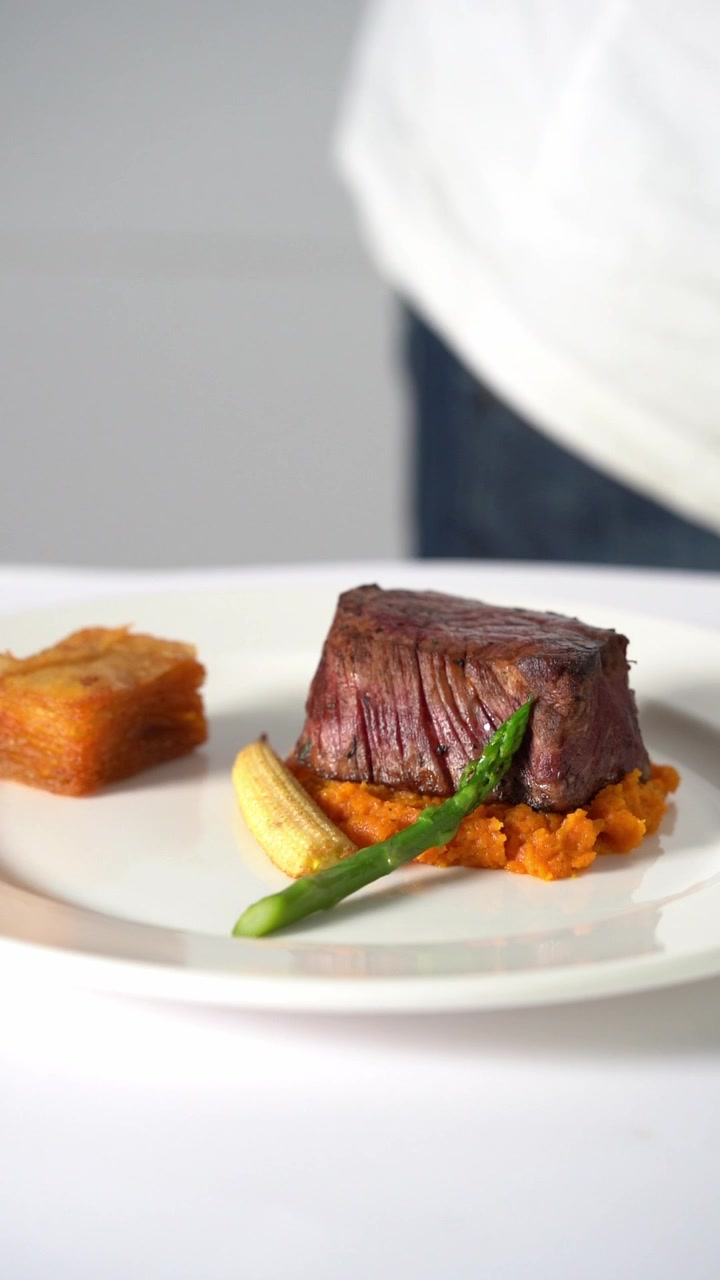 Uno chef che impiattava una succulenta bistecca di manzo alla griglia servita su purè di verdure cremoso in un piatto minimalista, primo piano, inquadratura di dettaglio
