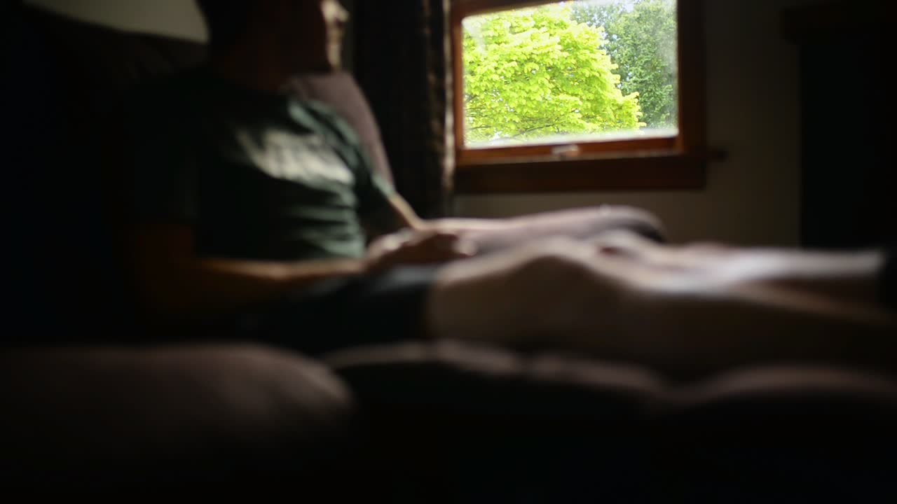 초점이 맞지 않는 어두운 거실에서 소파에 앉아 창밖을 내다보는 젊은 남자