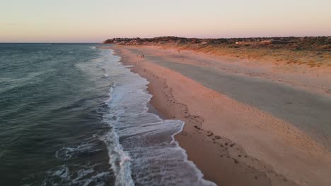 Port-Noarlunga-South-Australia,-Drone-flight-lifting-from-crashing-waves-to-see-a-family-playing-on-the-beach-in-the-distance