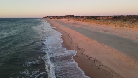 Port-Noarlunga,-Südaustralien,-Drohnenflug,-Der-Sich-Von-Tosenden-Wellen-Erhebt,-Um-In-Der-Ferne-Eine-Familie-Am-Strand-Spielen-Zu-Sehen