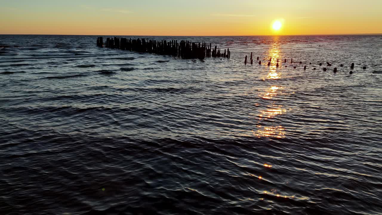 Old wooden pier jutting out into a calm ocean at sunset
