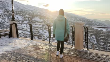 Tracking-shot-of-a-woman-walking-toward-a-fence-overlooking-the-snowy-Sierra-Nevada,-Spain