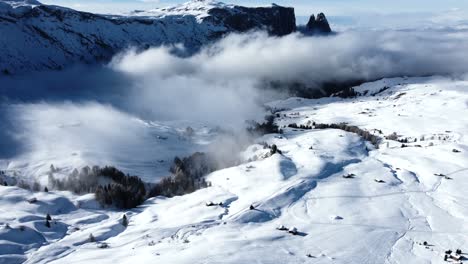 Flying-over-the-winter-scenery-in-the-Italian-Dolomites,-while-clouds-are-moving-in-front-of-the-peaks-on-a-sunny-day