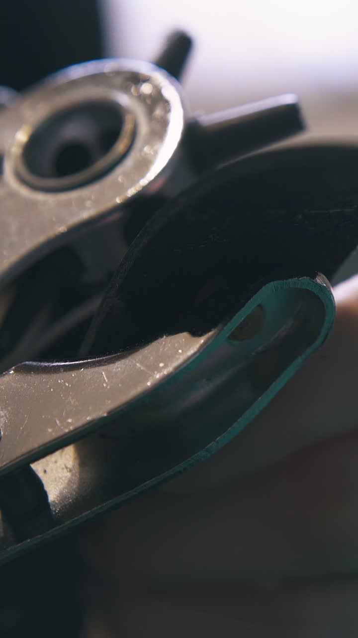 CU: Professional designer makes holes in black leather strip with special silver punch pliers close view